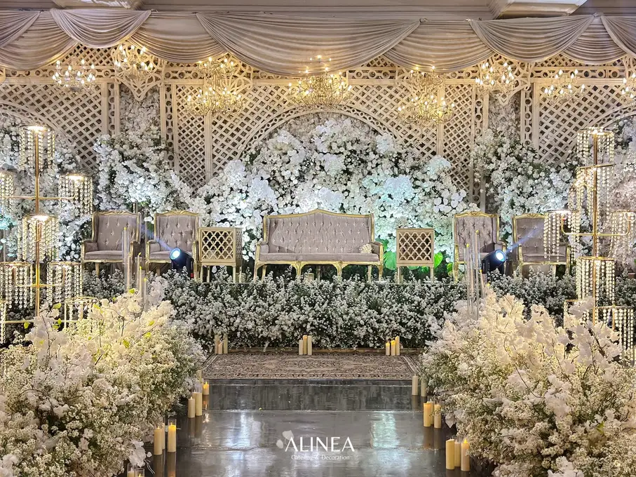 Pelaminan putih dengan bunga putih, kisi-kisi krem, dan deretan lampu gantung kristal. Dekorasi pernikahan Dinda & Ariq oleh Alinea.