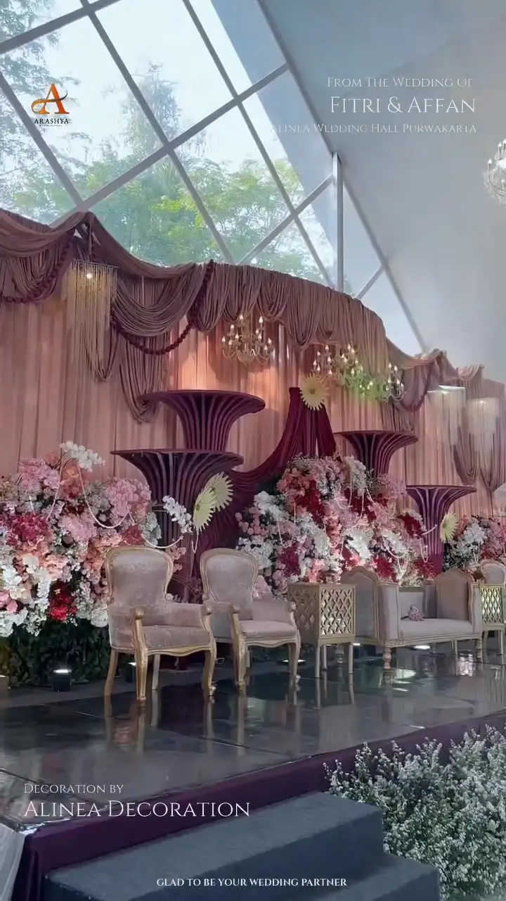 Pelaminan dengan kursi krem dan rangkaian bunga merah muda di Alinea Wedding Hall